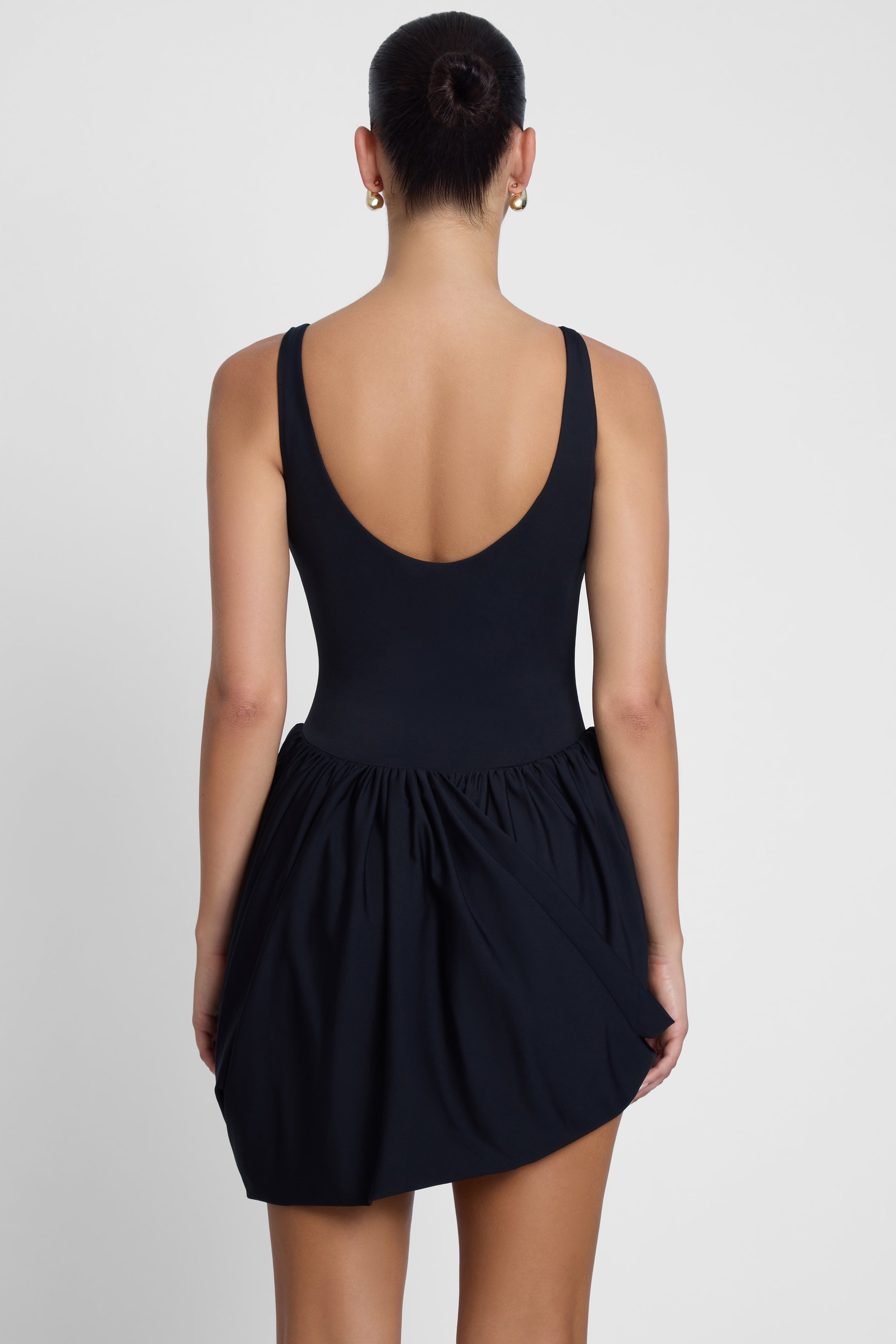 Model is wearing Dasia Sculpt Drape Mini Dress Black, back view.